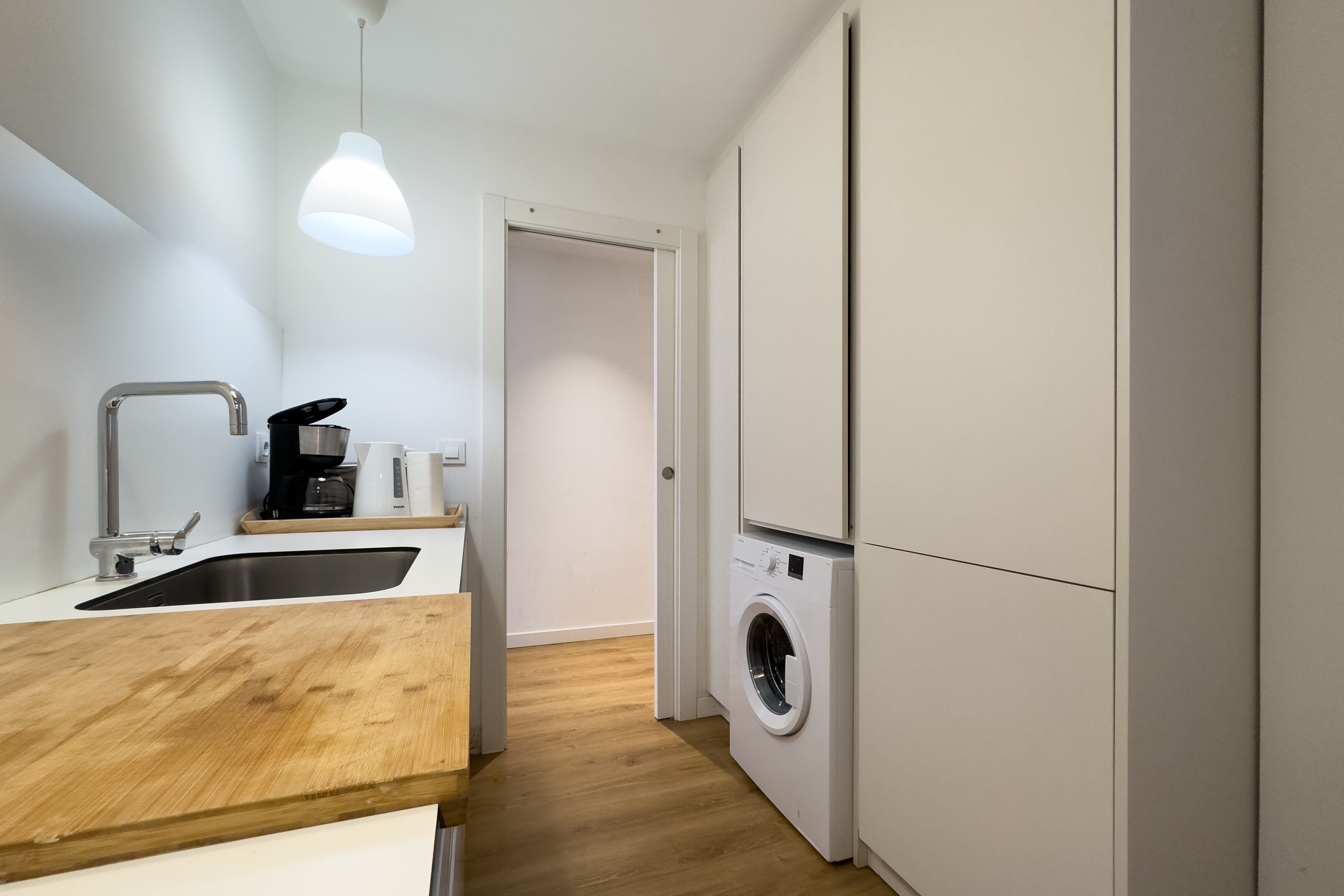 Una cocina moderna con encimera de madera, pileta de acero inoxidable y lavadora integrada.
