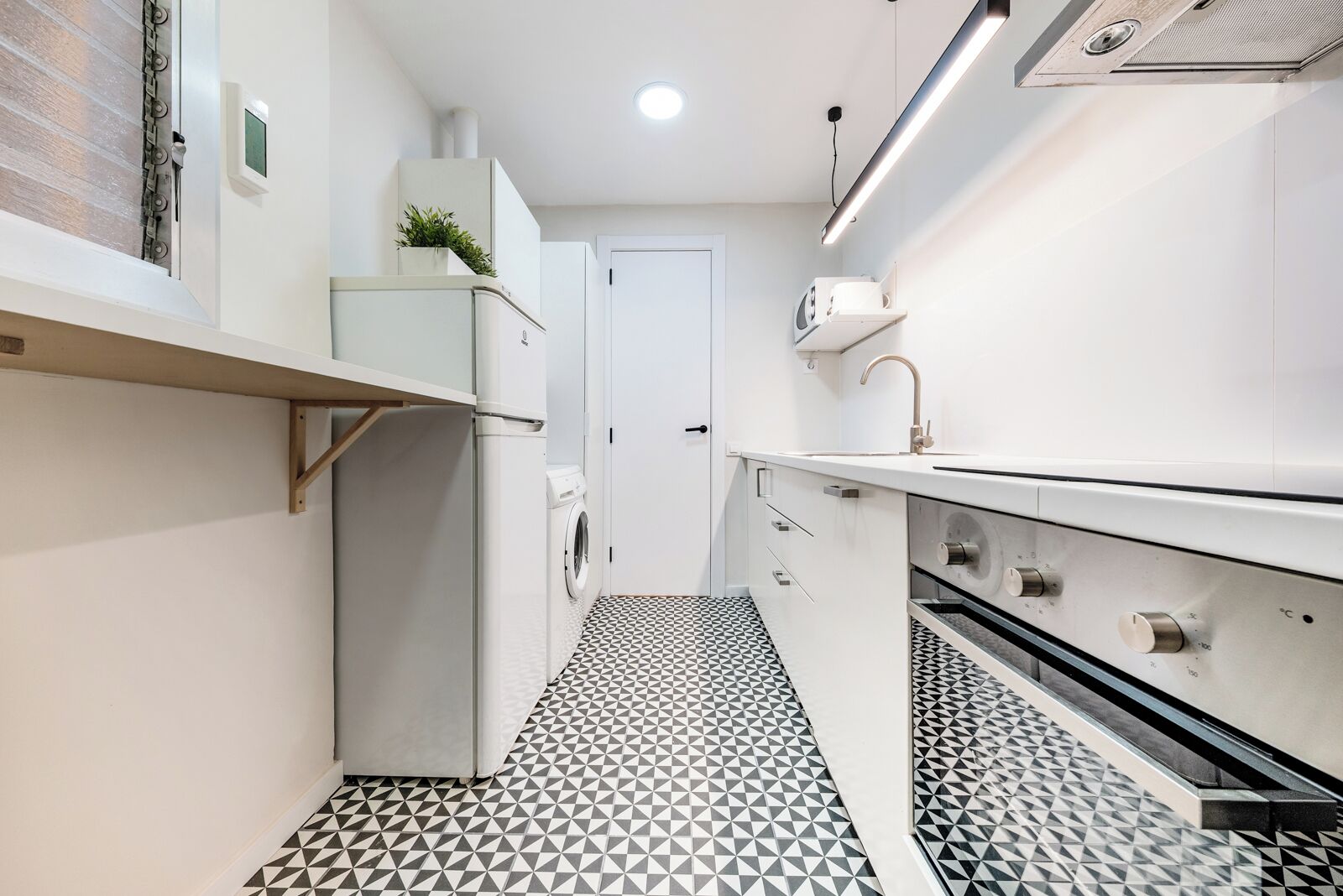 Una cocina estrecha con lavadora, microondas y fregadero.