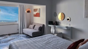 Een moderne hotelkamer met een bed, een bank, een bureau en uitzicht op de oceaan.