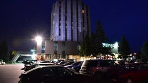 A parking lot with several cars and a building with a 'Bingo' sign. - Business Hotel Prijedor (Prijedor)