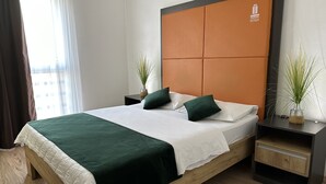 A neatly made bed with a green and white bedspread, two green pillows, and a wooden headboard with a logo. There are two bedside tables with plants and a small cabinet. - Business Hotel Prijedor (Prijedor)