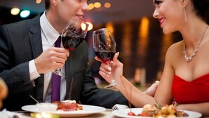 A couple toasting with wine glasses at a dinner table with candles, surrounded by plates of food. - Business Hotel Prijedor (Prijedor)