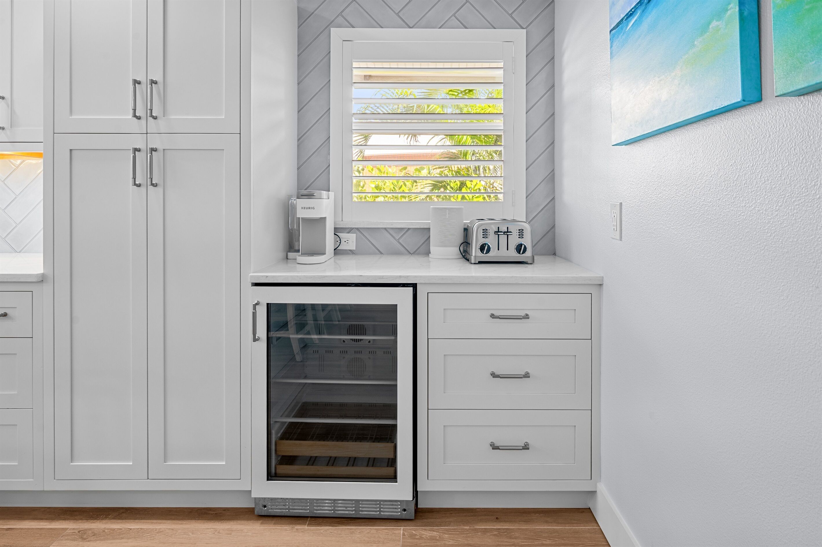 A kitchen with white cabinets, a built-in oven, and a window with blinds.