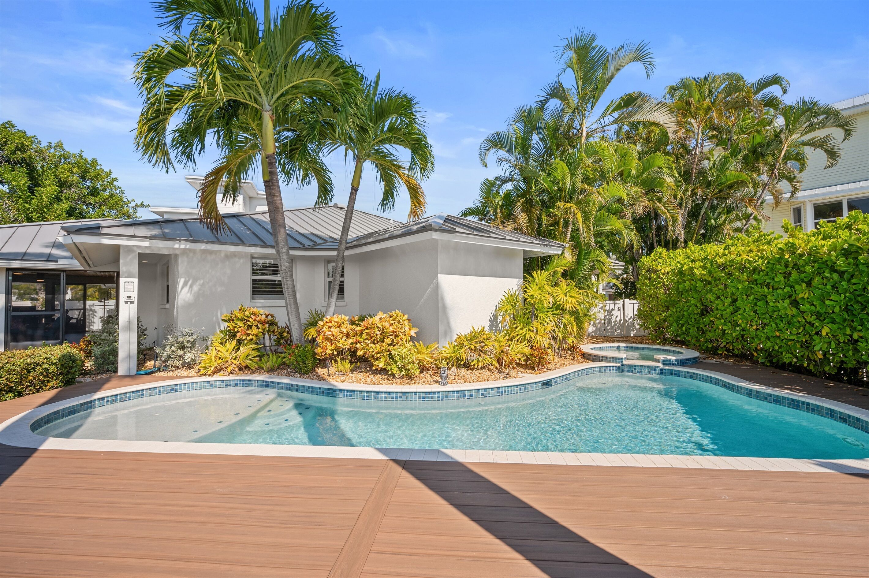 A modern house with a swimming pool, surrounded by tropical plants and palm trees.