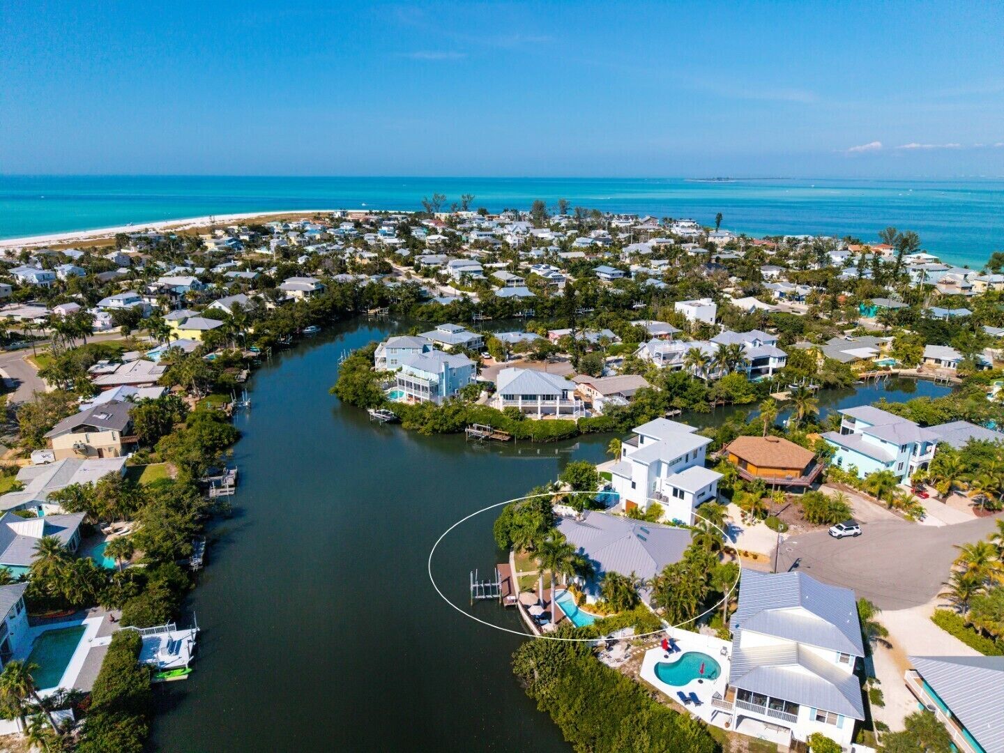 An aerial view of a coastal residential area with houses, a river, and a beach.