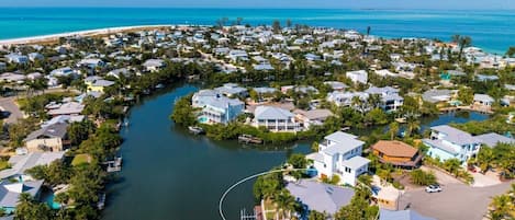 An aerial view of a coastal residential area with houses, a river, and a beach.
