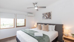 A bedroom with a bed, two windows, a ceiling fan, a wall-mounted air conditioner, and a framed picture.