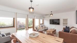 A modern living room with a wooden dining table, leather sofas, and a TV mounted on the wall.