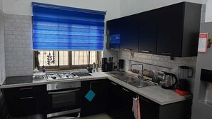 Eine moderne Küche mit schwarzen Schränken, einem Gasherd, einer Spüle und einem Fenster mit blauen Jalousien.