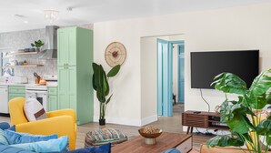 Un saló modern amb un sofà, una taula de centre i una televisió. Hi ha una zona de cuina amb armaris i una estufa.