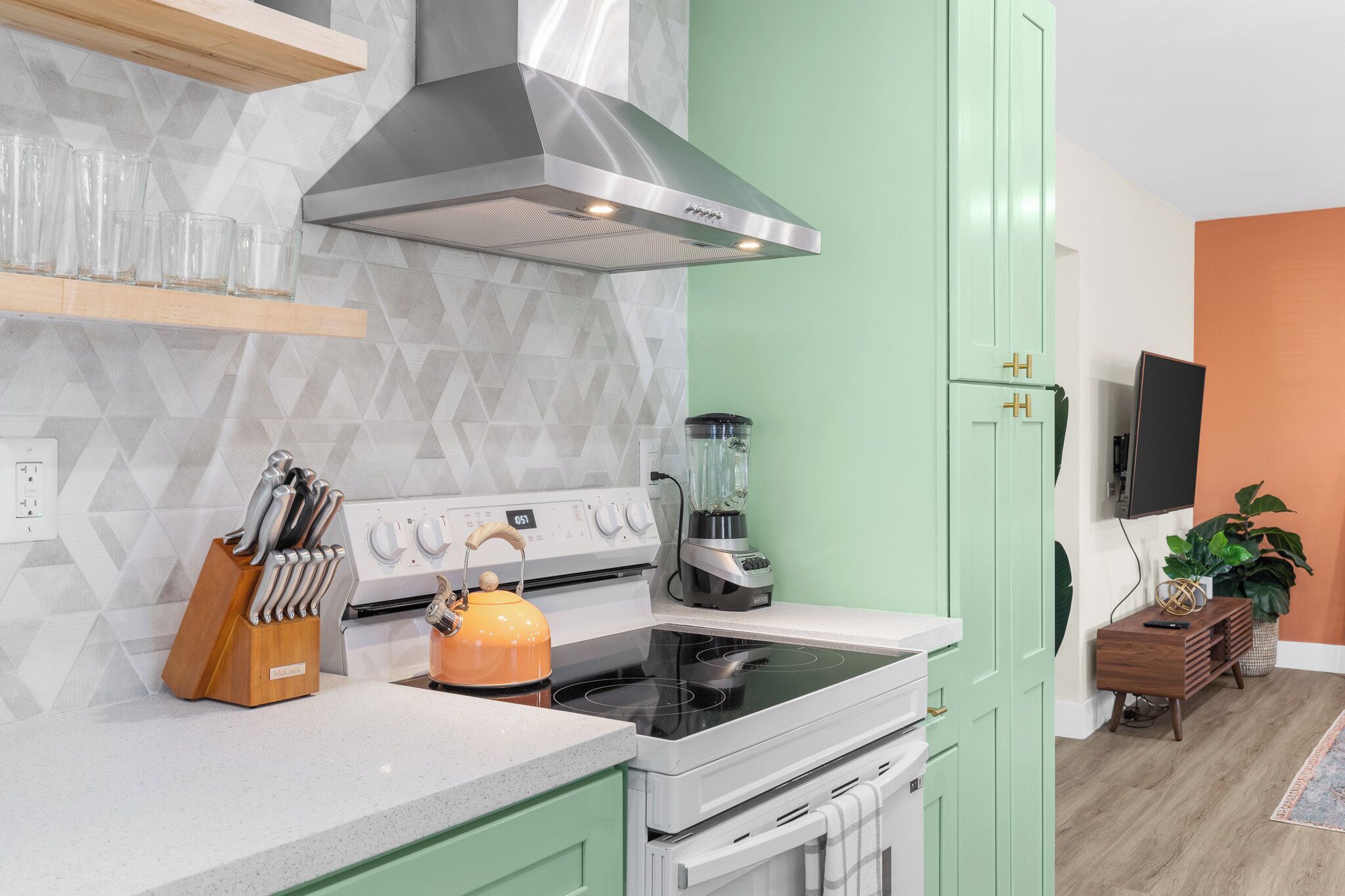 A modern kitchen with a gas stove, a built-in oven, a stainless steel range hood, and a blender on the counter.