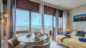 A hotel room with a bed, a dining table with chairs, a view of the sea, and a painting on the wall. - Alvor Bay Dream by Interhome (Alvor)