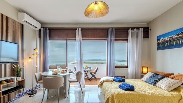 A modern hotel room with a bed, a dining area, a TV, and a balcony with a view. - Alvor Bay Dream by Interhome (Alvor)