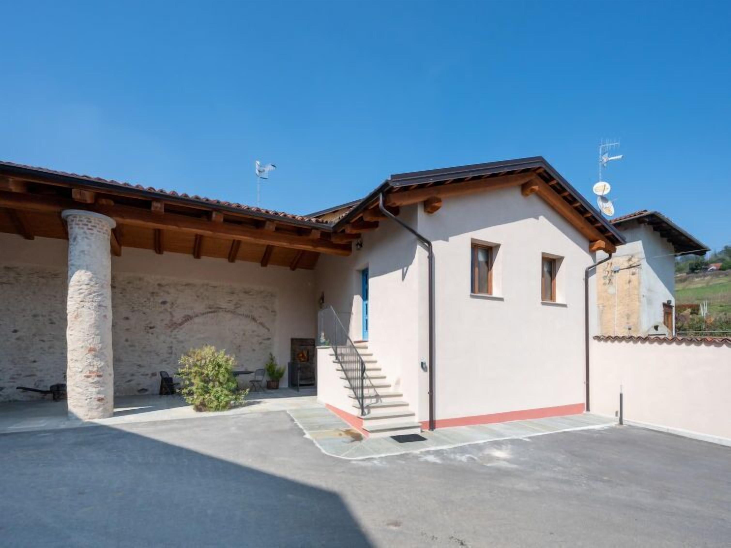 A two-story building with a stone facade, wooden beams, and a tiled roof. There is a staircase leading to the upper floor and a small balcony.