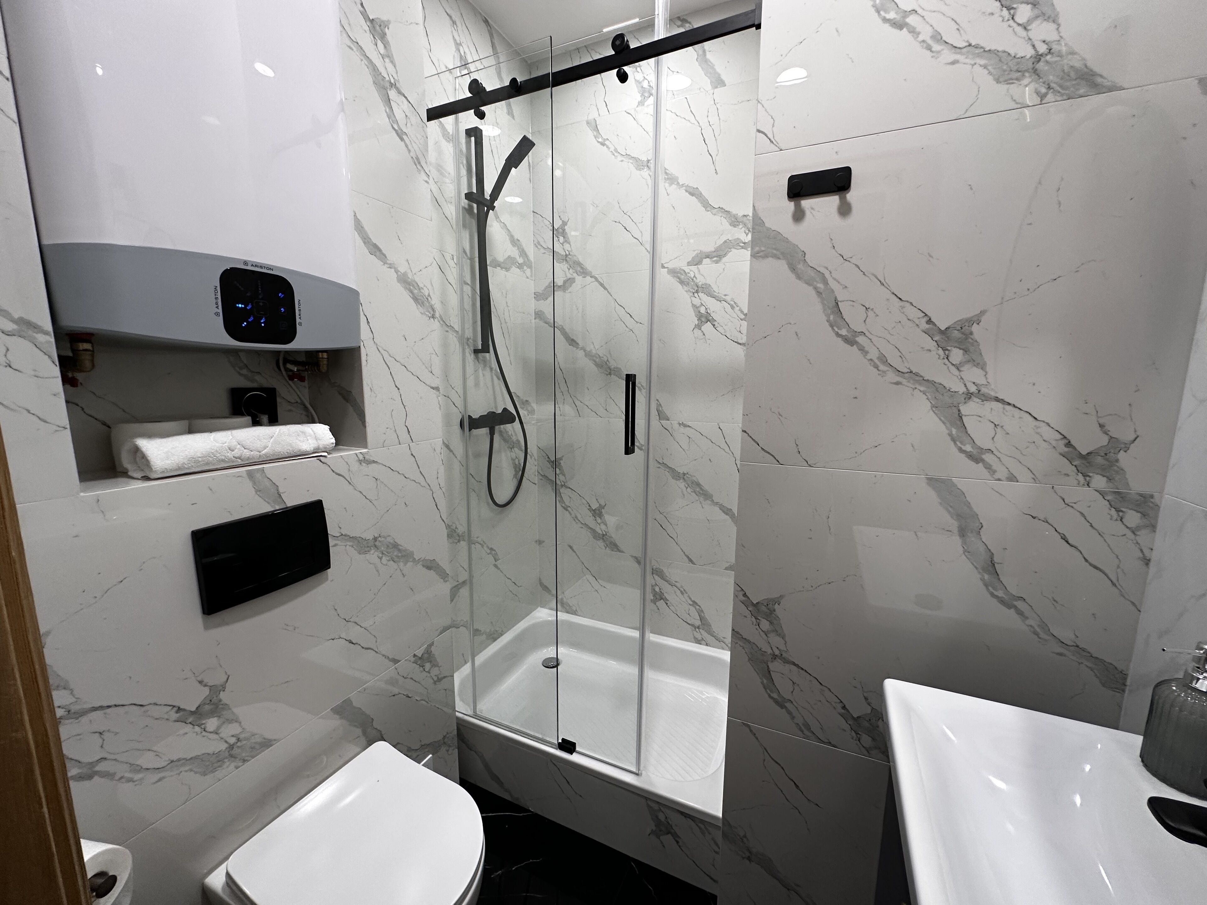 A modern bathroom with a glass-enclosed shower, a toilet, and a sink.