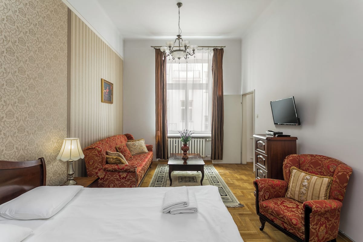 A hotel room with a bed, a sofa, a chair, a television, and a window with curtains.