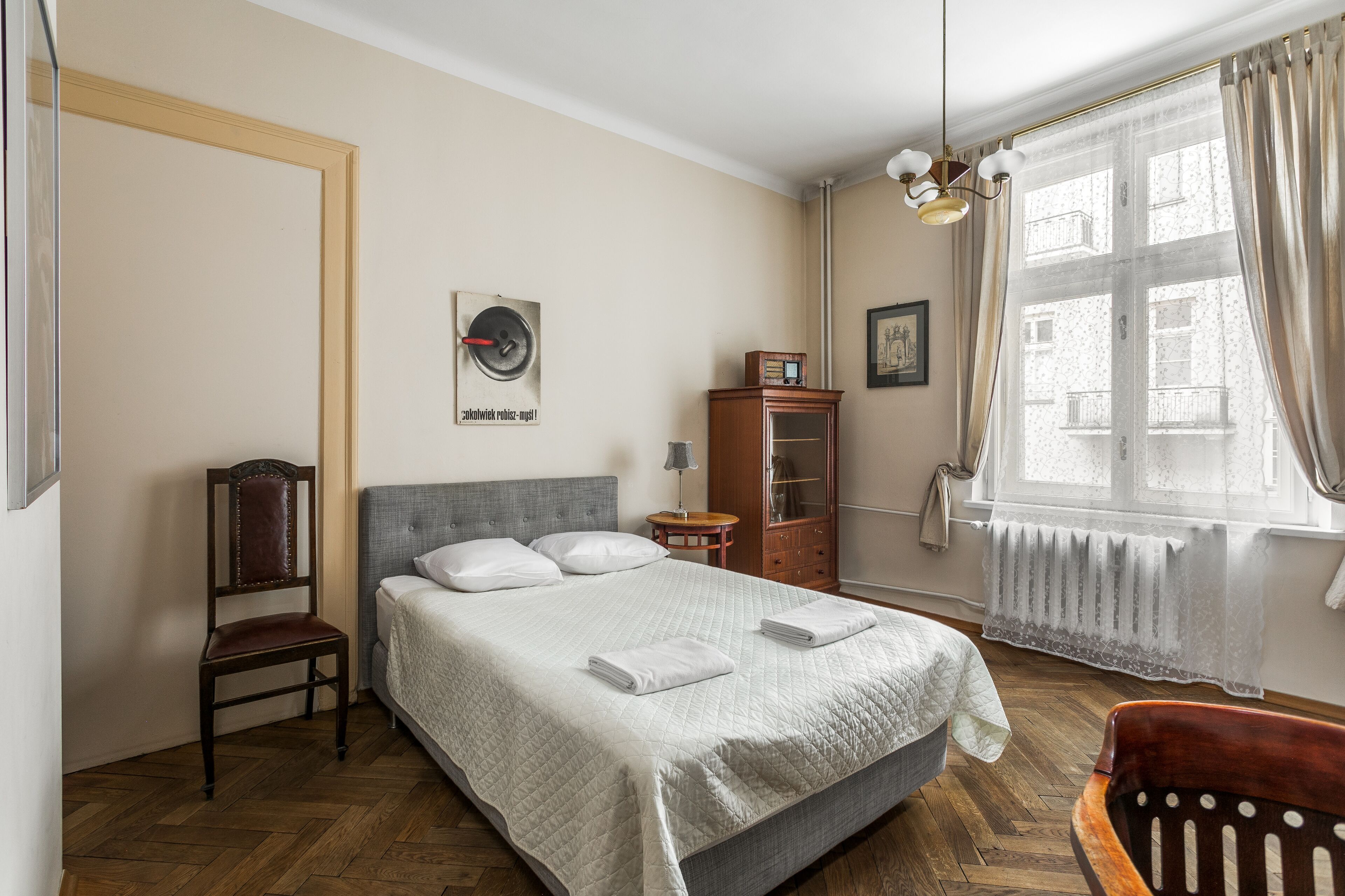 Un dormitorio ordenado con cama, una silla, un armario y un radiador.