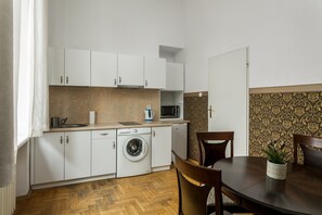 Cocina compacta con armarios blancos, lavadora, microondas y comedor con mesa y sillas.