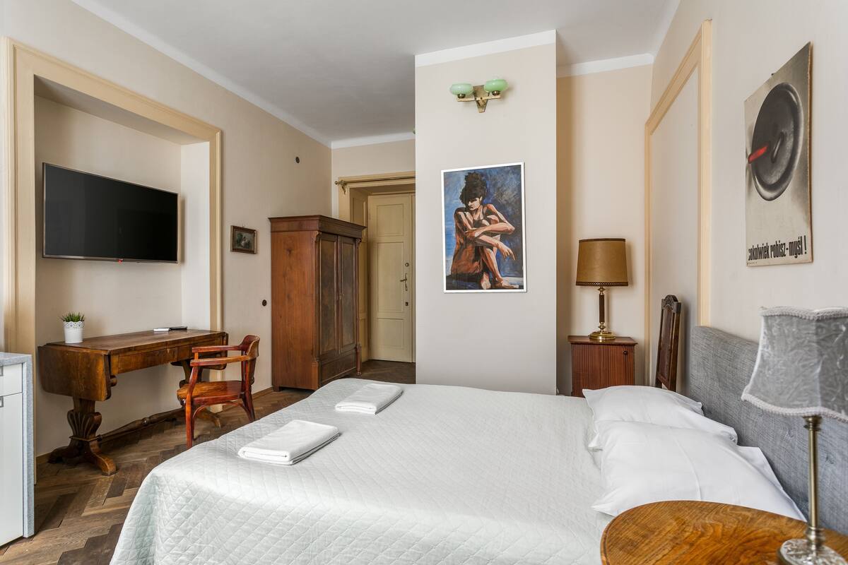 A hotel room with a bed, a desk, a television, a wardrobe, and a painting on the wall.