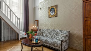 A living room with a patterned sofa, a wooden coffee table with decorative items, a staircase, and a wall-mounted picture frame.