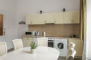 Une cuisine compacte équipée d’un four à micro-ondes, d’une cuisinière, d’un four et d’un lave-linge. On y trouve une table à manger avec des chaises et une plante en pot.