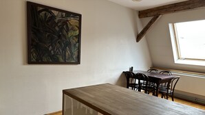 A dining area with a wooden table and chairs, a painting on the wall, and a window with natural light.