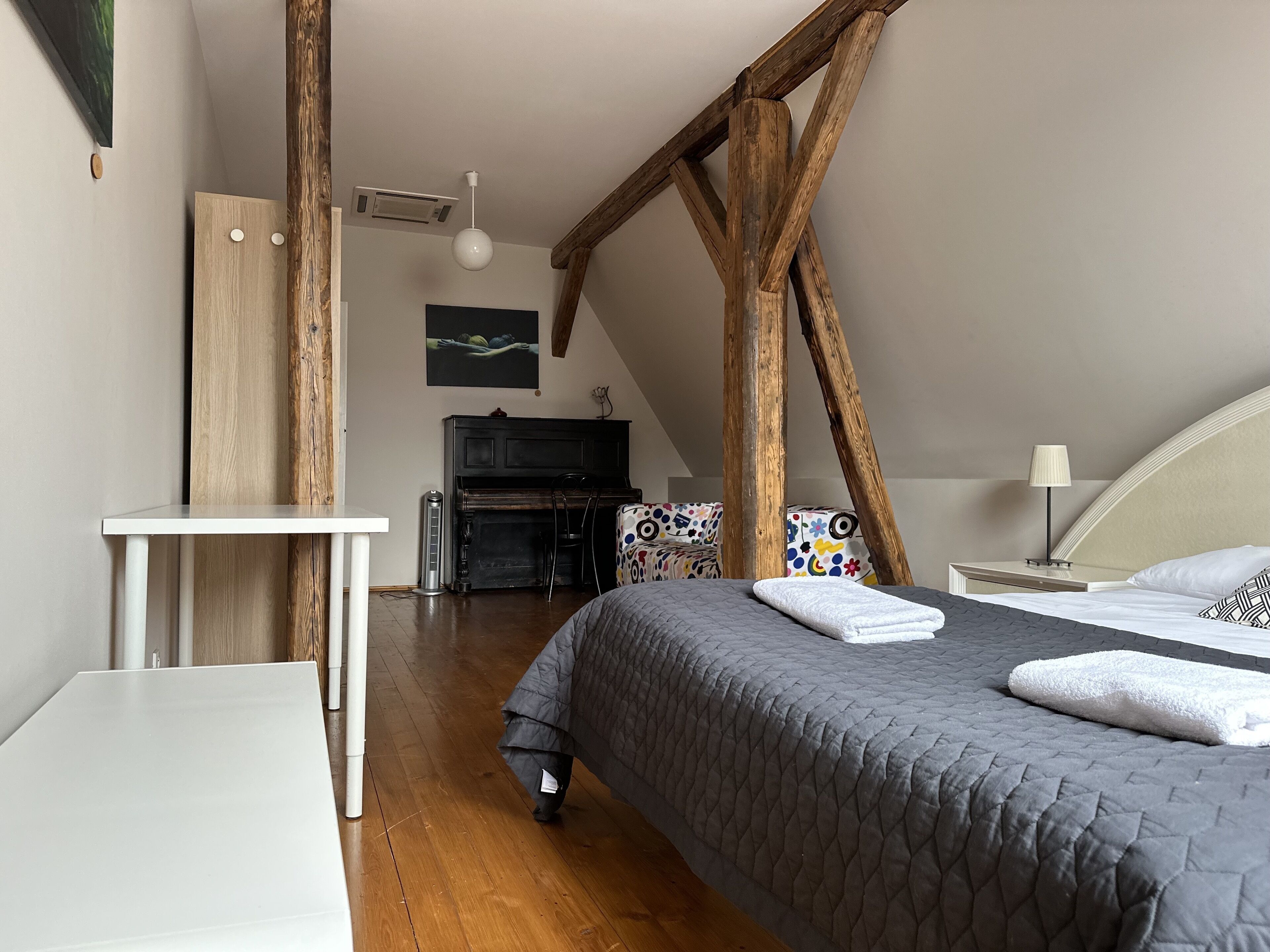 A bedroom with a bed, a desk, a chair, a piano, and a ceiling fan.