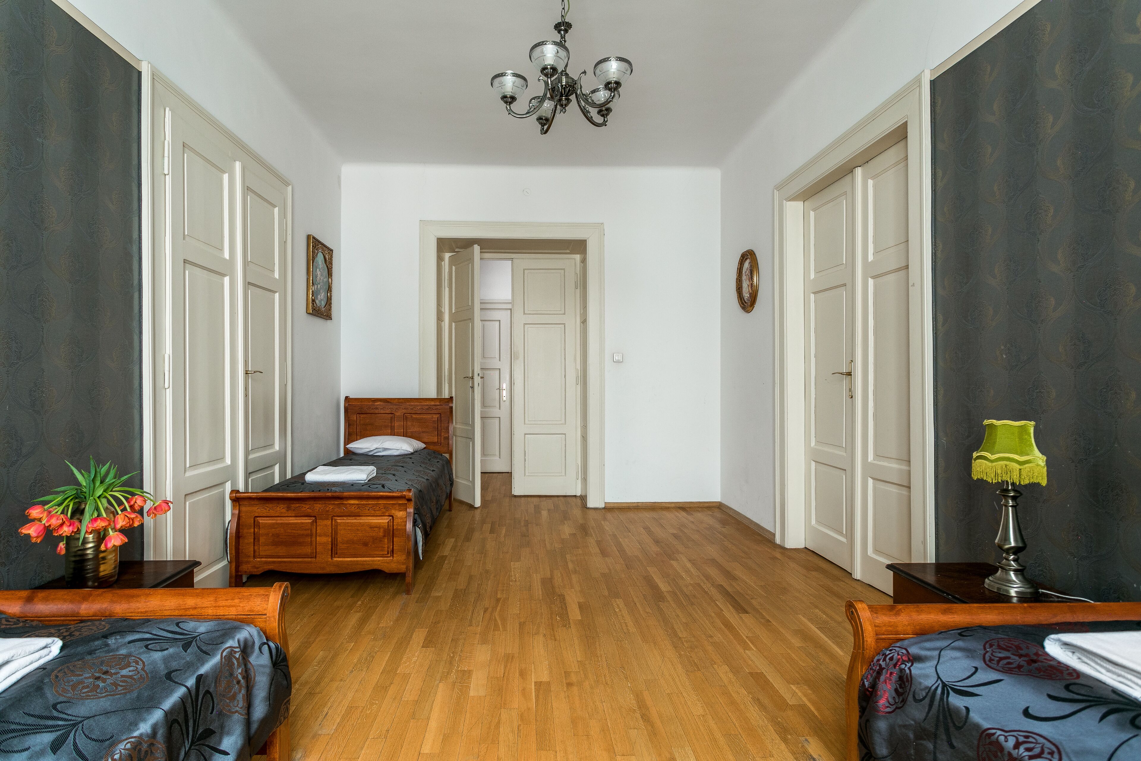 A bedroom with two wooden beds, a wooden dresser, a nightstand, a green lamp, and a potted plant.