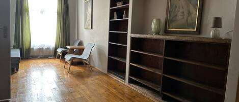 A room with wooden flooring, a desk, two chairs, a bookshelf, and a painting on the wall.