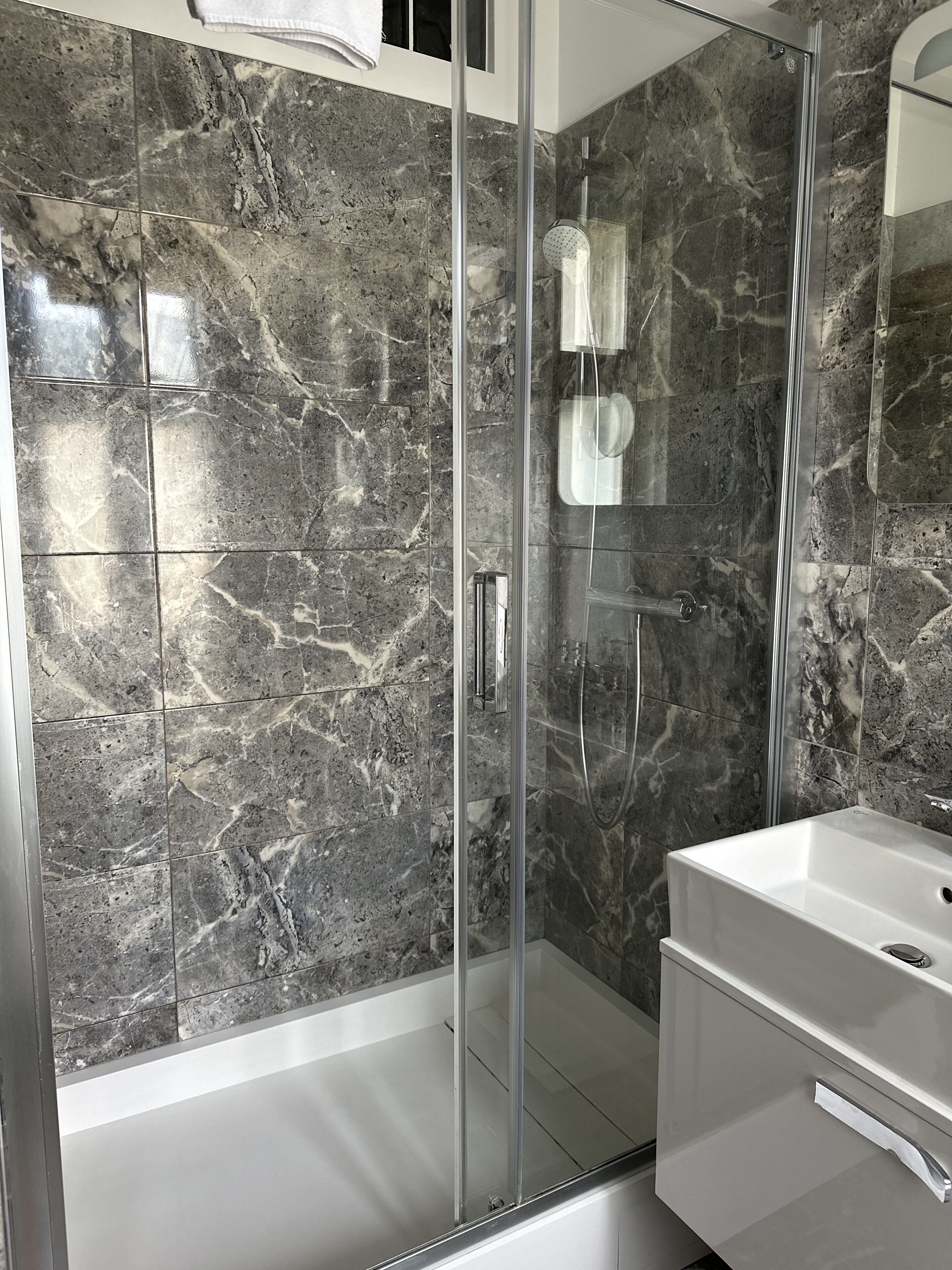 A modern bathroom with a glass-enclosed shower, marble walls, and a white vanity.
