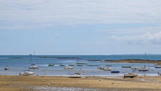 A beach with several boats anchored in shallow water, a sandy shore, and a distant shoreline with a breakwater. - Le Large by Interhome (Saint Philibert)