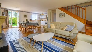 A spacious living room with a sofa, a coffee table, and a dining area with chairs and a table. A staircase leads to an upper level. - Le Large by Interhome (Saint Philibert)