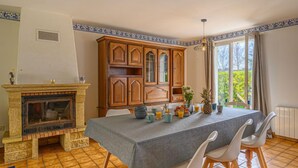 A dining area with a stone fireplace, wooden cabinets, and a table set for four. - Le Large by Interhome (Saint Philibert)