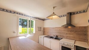 A kitchen with a wooden countertop, white cabinets, a stove, and a window with a view of greenery. - Le Large by Interhome (Saint Philibert)