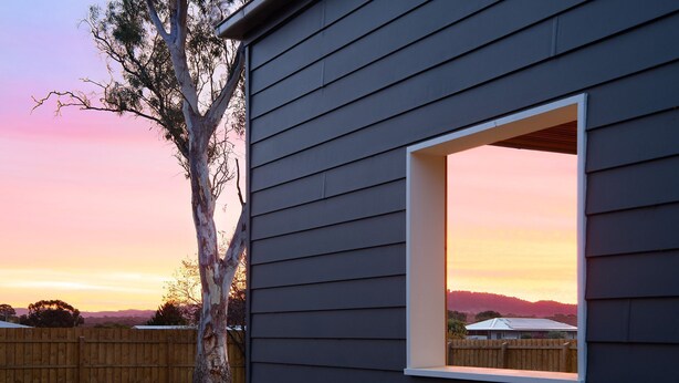 Una casa con una finestra che si apre su una vista al tramonto, una recinzione in legno e un albero.