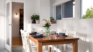 Zona pranzo con tavolo in legno apparecchiata per quattro persone, sedie bianche e un vaso con fiori.