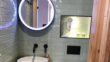 A bathroom with a wooden vanity, a round mirror, a handheld showerhead, and a toilet.
