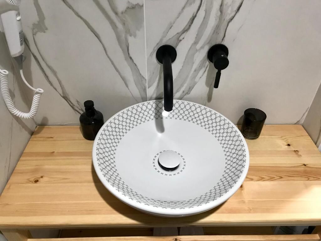 Un baño con un lavamanos blanco, una pared de mármol y un mueble de tocador de madera.
