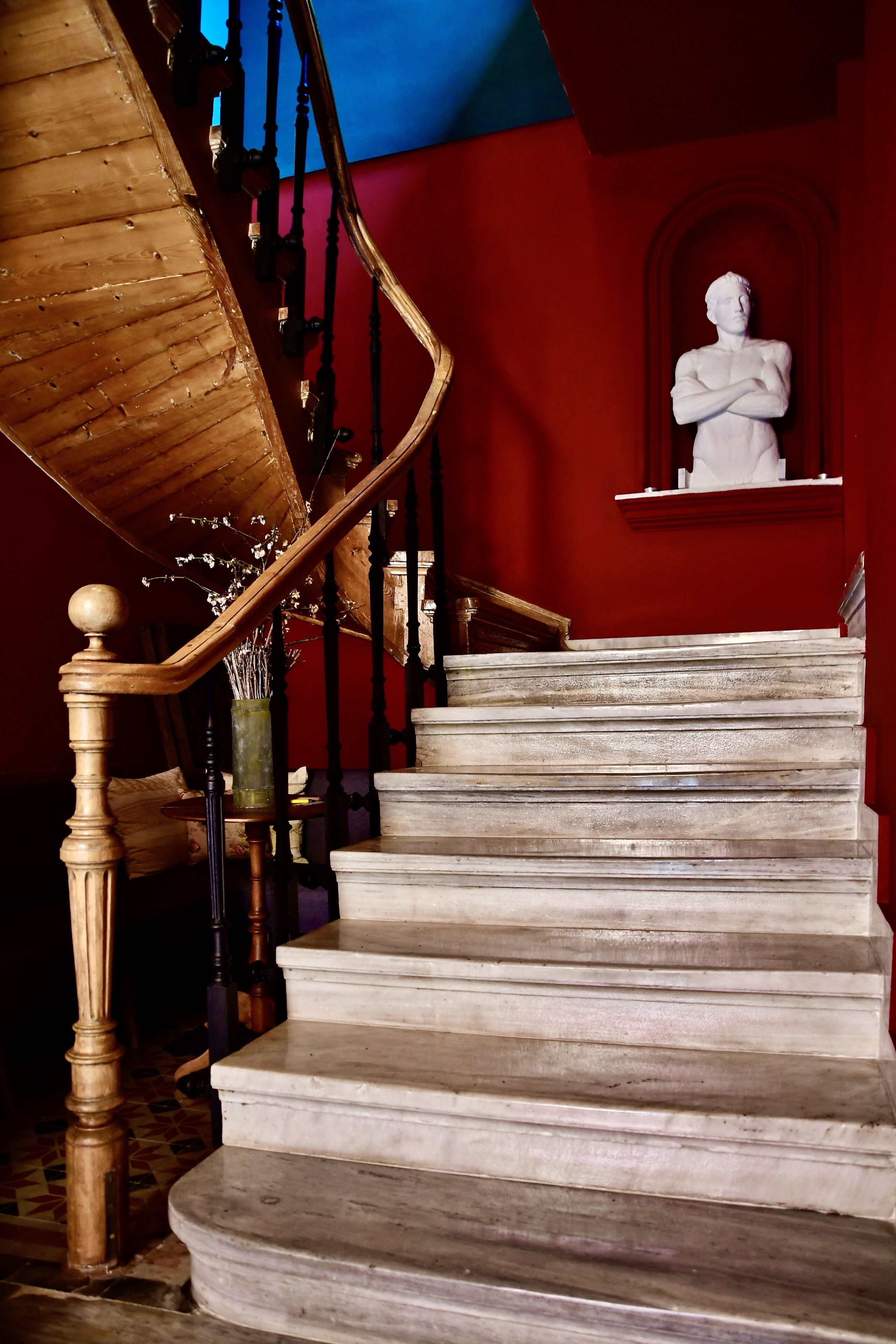 Una escalera de mármol con barandilla de madera y una estatua en la parte superior.