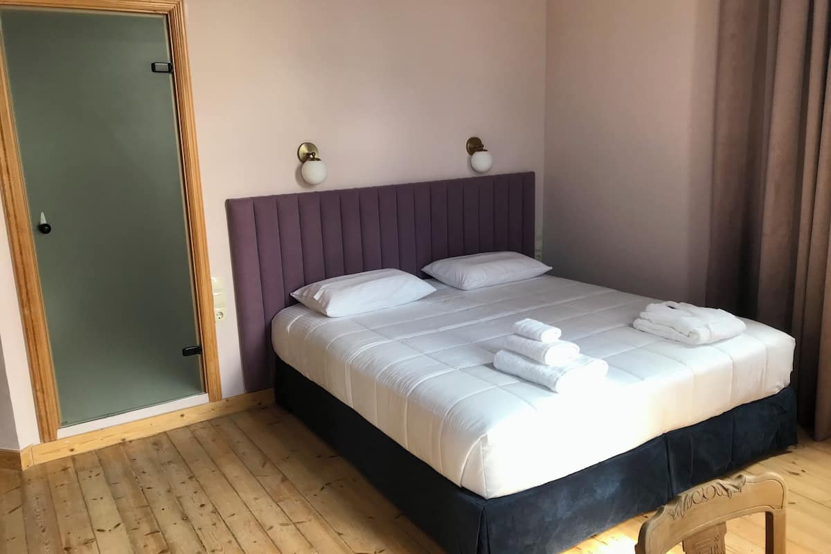 A bedroom with a bed, pillows, a nightstand, a chair, and a door.