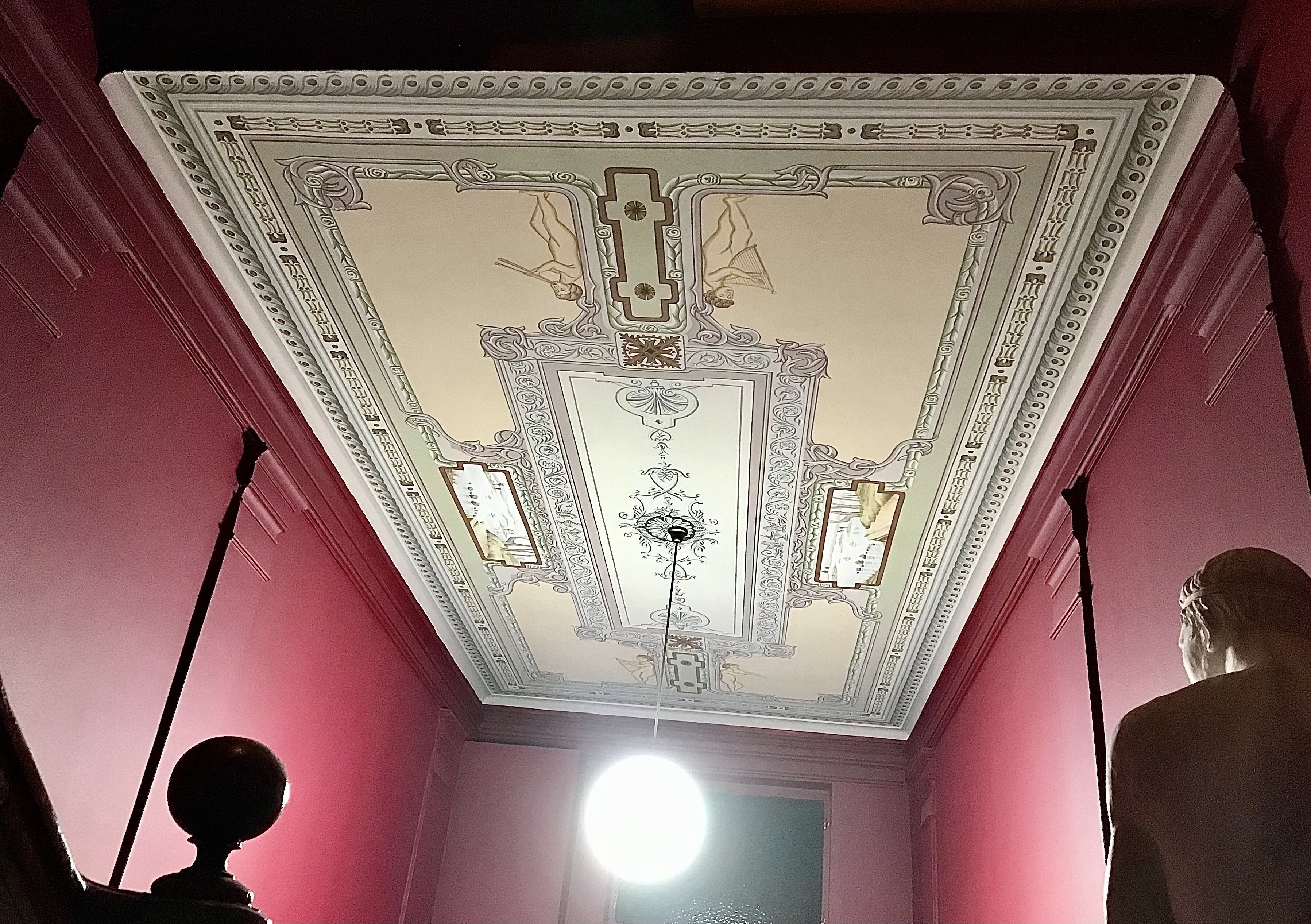 Ein Zimmer mit dekorierter Decke, einer Chandelier und einer Statue.