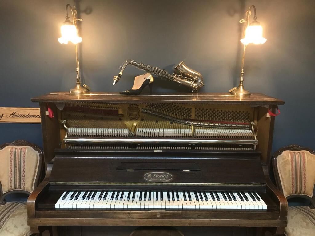 A grand piano with two upright stands, a saxophone, and a sign reading "Aristodemus".