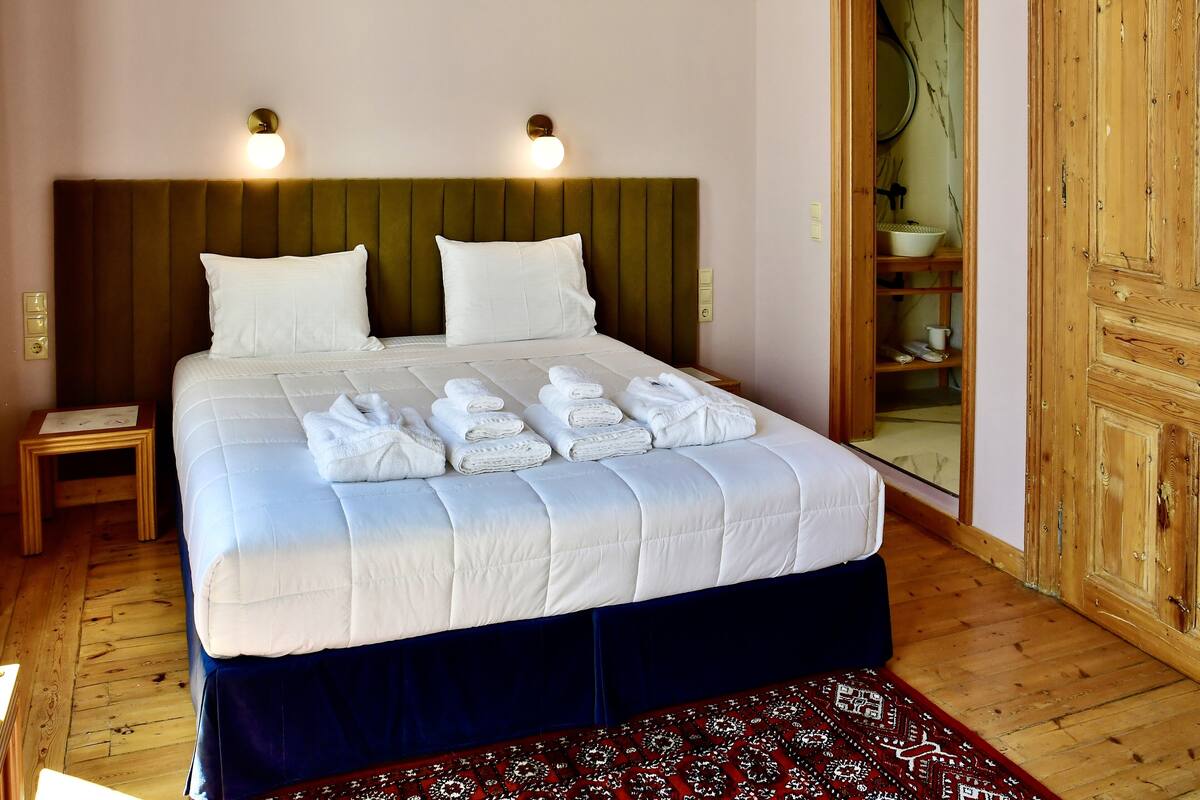 A neatly made bed with white linens and towels, a wooden headboard, and two wall-mounted lights.
