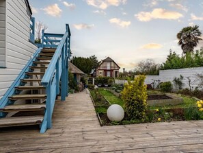 A wooden deck leading to a house with a blue staircase, surrounded by a garden with various plants and a large spherical object.