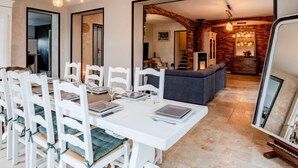 Un comedor con sillas blancas y una mesa dispuesta para cuatro personas, una chimenea y una pared de piedra al fondo.