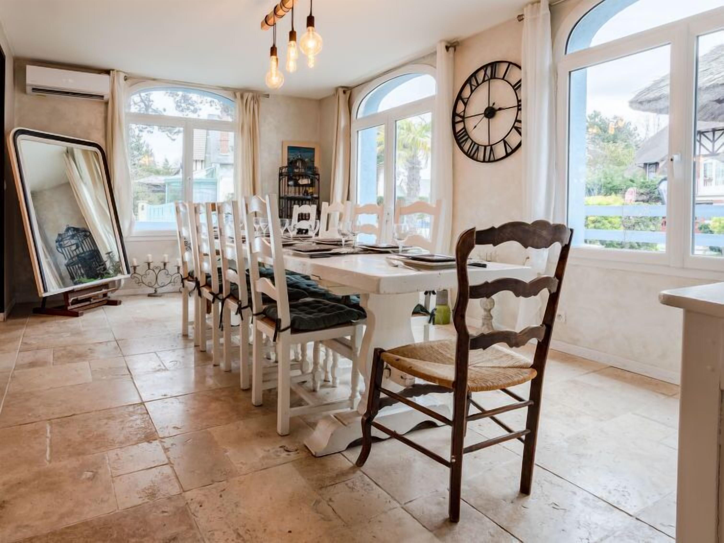 A dining area with a long table, white chairs, and a large wall clock.