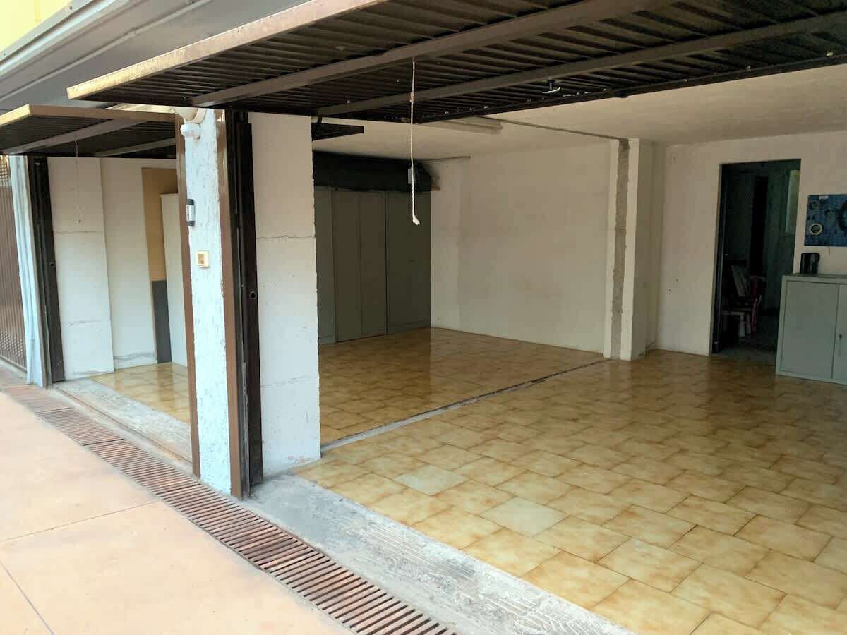 Une pièce vide avec un sol carrelé, des piliers en béton et un plafond avec des poutres apparentes.