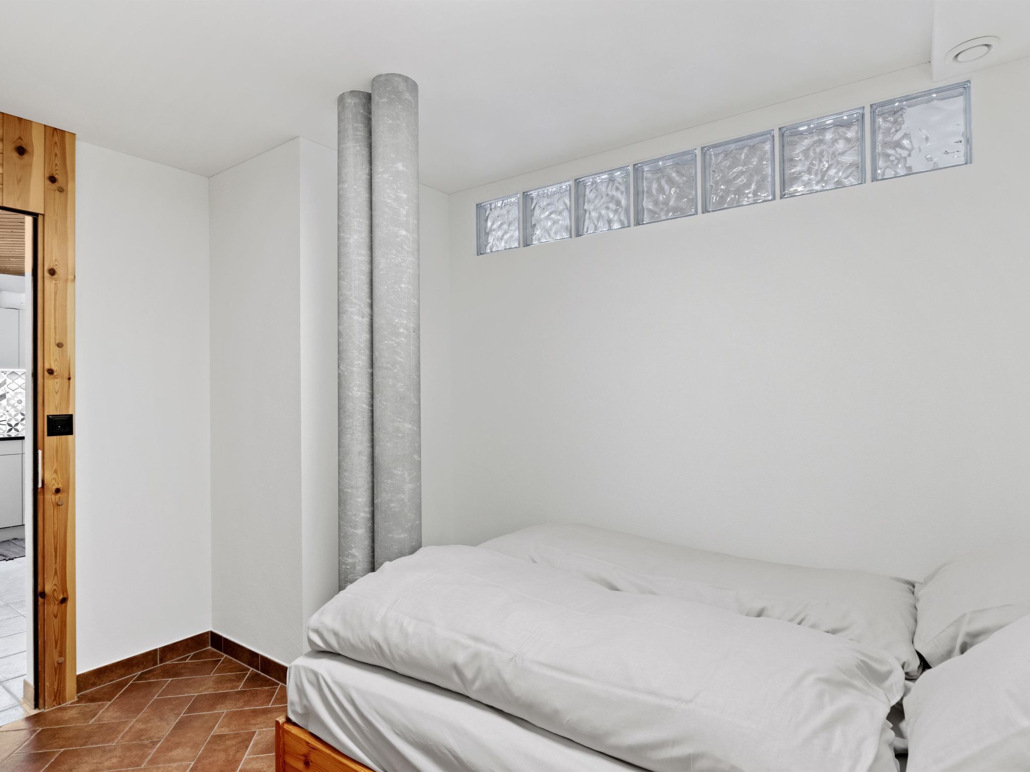 A bedroom with a bed, a wooden door, a white wall, and a window.