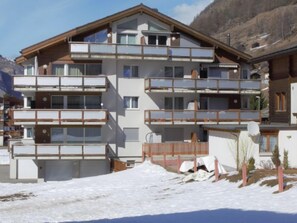 Un immeuble à plusieurs étages dot é de balcons, vraisemblablement un hôtel ou un ensemble d’appartements, entouré de neige et de montagnes.