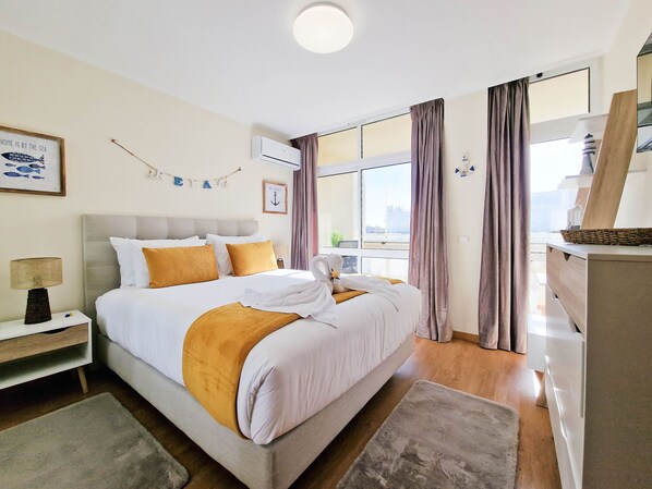 A hotel room with a large bed, a nightstand, a lamp, a window with curtains, and a view of the city.